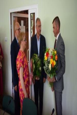 Grupka ludzi składa życzenia i wręcza kwiaty mężczyźnie