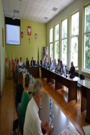 Duża sala, w której siedzą ludzie, przy długich stołach- obrady w czasie Sesji