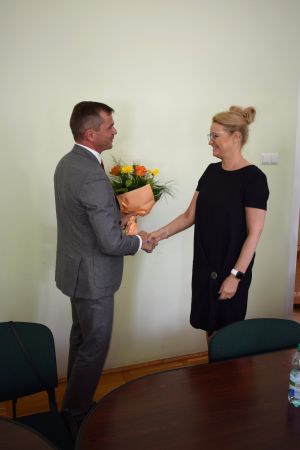 Kobieta w czarnej sukience składa gratulacje i wręcza kwiaty mężczyźnie