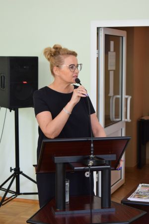 Kobieta w czarnej sukience, przemawia stojąc na mównicy