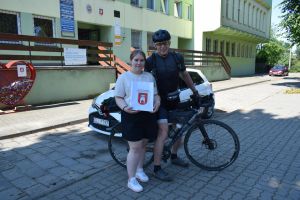 Rowerzysta pozujący do zdjęcia z kobietą, która trzyma w dłoni torbę z herbem gminy