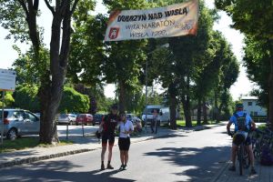 Dwójka rowerzystów- kobieta i mężczyzna, pozują do zdjęcia na drodze, pod banerem powitalnym.