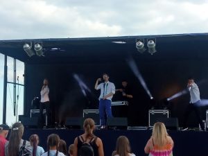 Grupka ludzi obserwujących występ piosenkarza z dwoma tancerzami na scenie