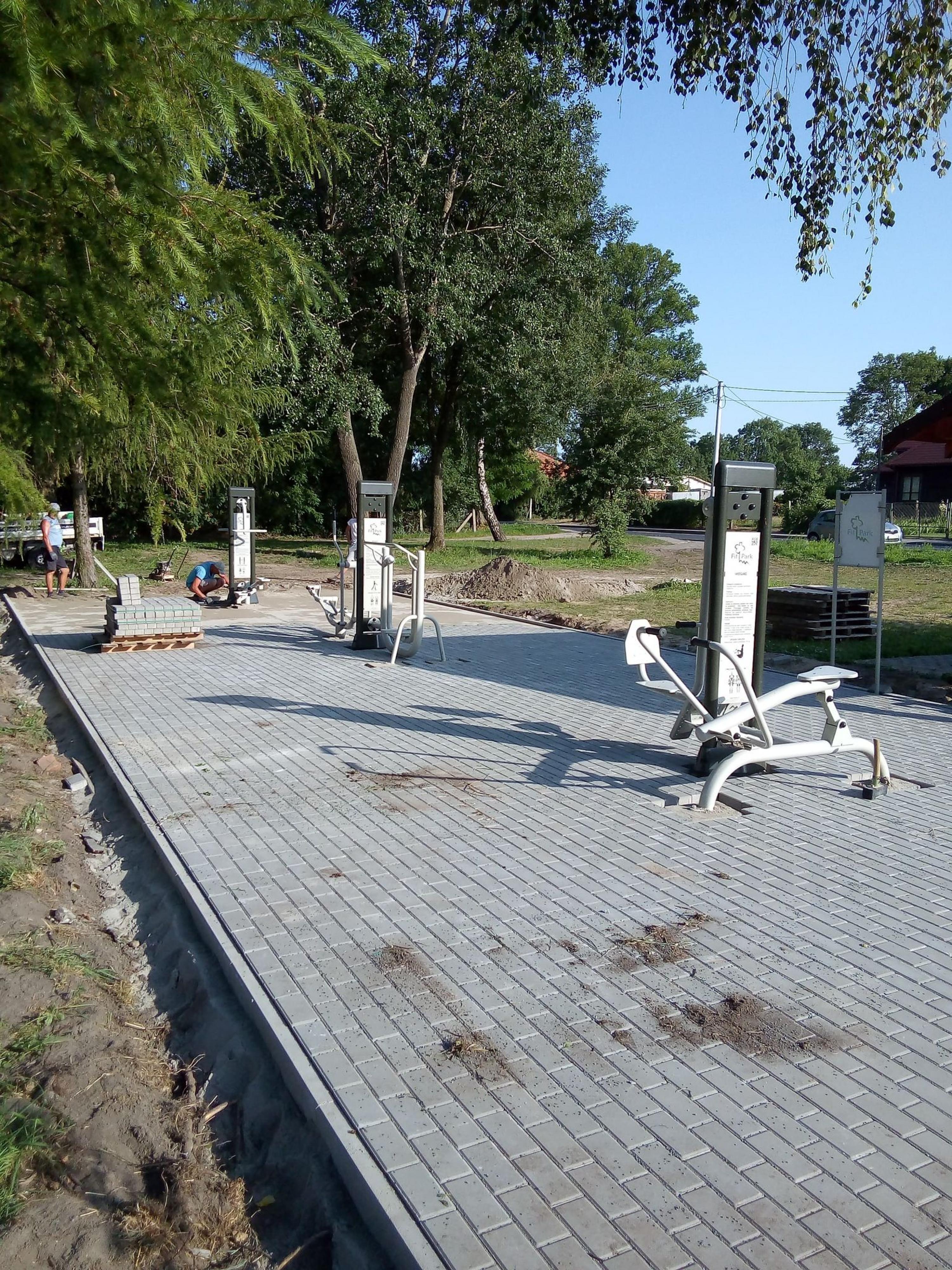 Plac, wyłożony kostką brukową, na której znajdują się elementy siłowni zewnętrznej