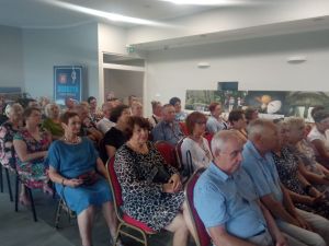 Przestronna sala, wypełniona ludźmi siedziącymi na krzesłach