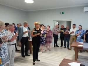 Grupa osób, stojąca w przestronnej sali z kieliszkiem wina w ręku