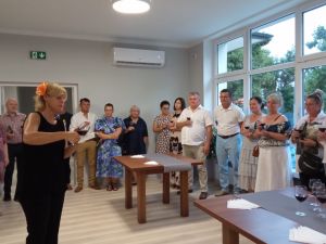 Grupa osób, przyglądająca się jak jedna z pań serwuje wino