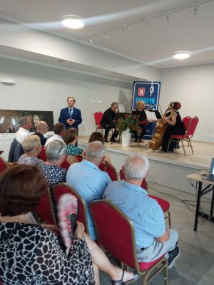 Grupa osób, stojąca w przestronnej sali z kieliszkiem wina w ręku