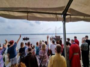 Tłum ludzi pod namiotem machający do odpływajacej barki