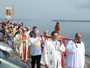 Orszak pielgrzymkowy, idący wzdłuż rzeki, na czele orszaku duchowni niosący drewnianą figurę