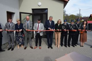 Kilkoro ludzi przecina symboliczna wstęgę na tle nowo wyremontowanej świetlicy wiejskiej