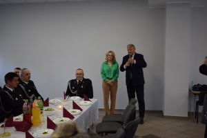 Mężczyzna i kobieta przemawiają do zgromadzonych w dużej sali osób, siedzących za zastawionymi stołami