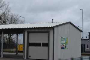 Część budynku głównego PSZOK, z widoczną boczna elewacją, na której umieszczona została tablica edukacyjna, informujaca o...