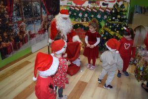 Mikołaj odwiedzający uczniów i przedszkolaków i częstujący ich słodyczami z czerwonego worka