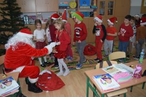 Mikołaj odwiedzający uczniów i przedszkolaków i częstujący ich słodyczami z czerwonego worka