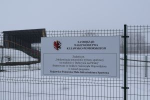 Tablica informacyjna umieszczona na zielonym ogrodzeniu z siatki