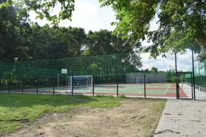 Widok boiska z ogrodzeniem i ułożonym chodnikiem z kostki brukowej