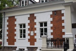 Beżowa elewacja dworku w połączeniu z czerwonymi cegłami