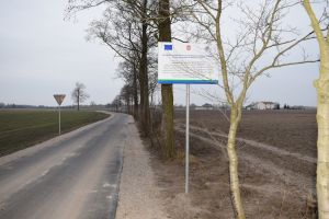 Tablica informacyja z logo Unii Europejskiej informująca o kwocie dofinansowania modernizacji na tle nowej drogi