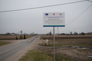 Tablica informacyja z logo Unii Europejskiej informująca o kwocie dofinansowania modernizacji na tle nowej drogi