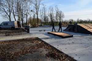 Betonowy plac, na którym pracownicy montują drewniane elementy skateparku