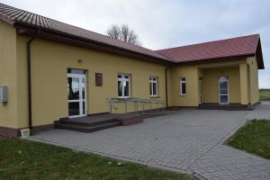 Odnowiony budynek OSP w Grochowalsku,żółta elewacja, widoczne także wejście do budynku oraz ułożona kostka brukowa przed...