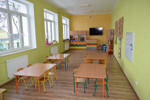 Sala lekcyjna w kolorze ścian zielono-żółtym wraz z wyposażeniem-ławki, krzesła, szafki, na głównej ścianie telewizor